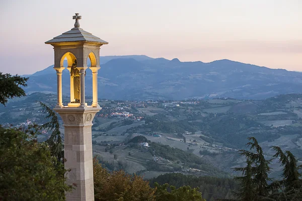 San Marino városának panorámája, háttérben a hegyekkel és a naplementével.