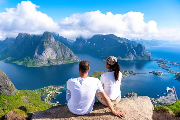 Egy pár ül a hegytetőn, csodálva a norvég fjordok lélegzetelállító panorámáját.