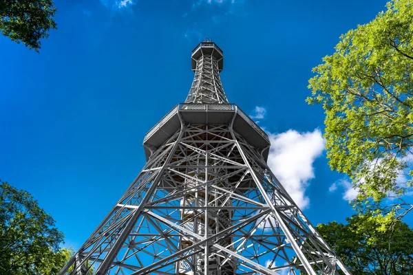 A Petrin-kilátó torony Prágában, zöld fák között, kék éggel.