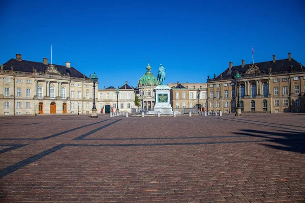 A Koppenhága központjában található Amalienborg palota, napfényben ragyogó épületekkel és szoborral.